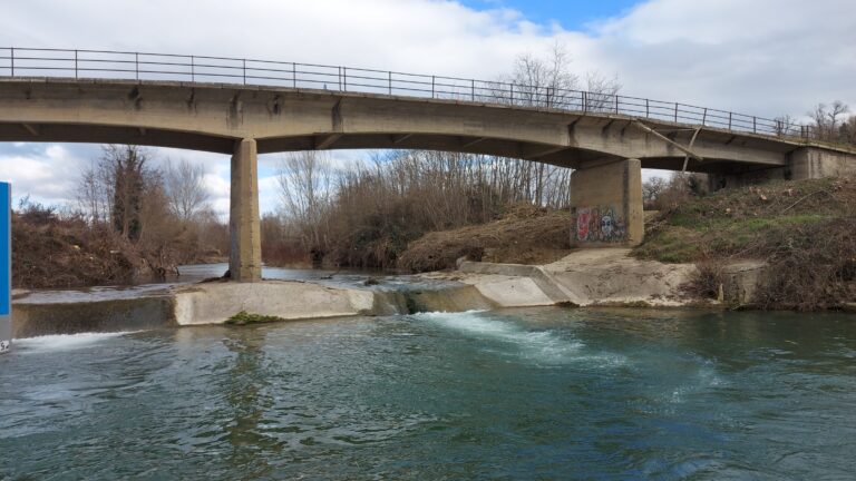 Immagine di un ponte di cemento su un fiume, catturata per il rilievo tramite drone, evidenziando la necessità di ispezione e valutazione della struttura.